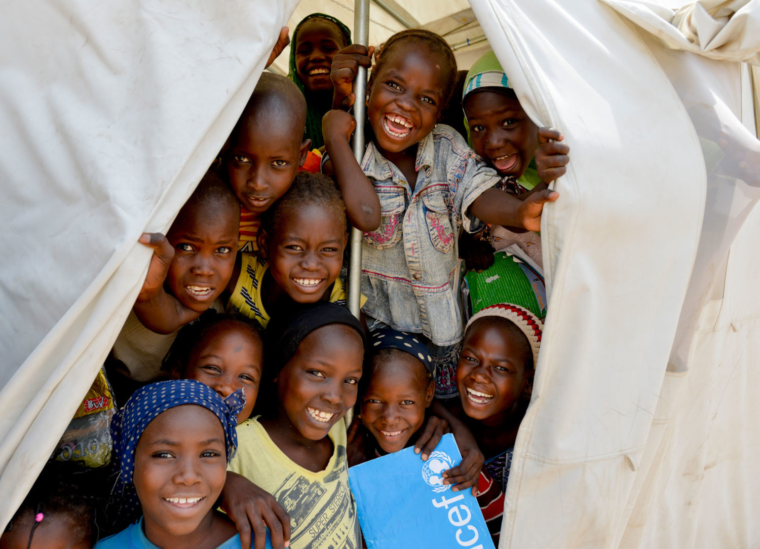 Remember someone special with a gift in memory to help keep children safe, like these children smiling in a Unicef-supported tent in Nigeria. Unicef 2015 Rich