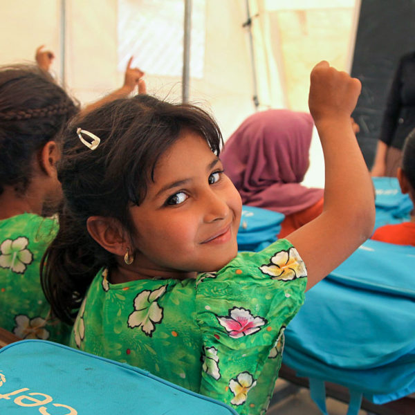 A young girl raises her hand to answer a question in a tented classroom at a camp for internally displaced in Iraq. Unicef 2016 Khuzaie