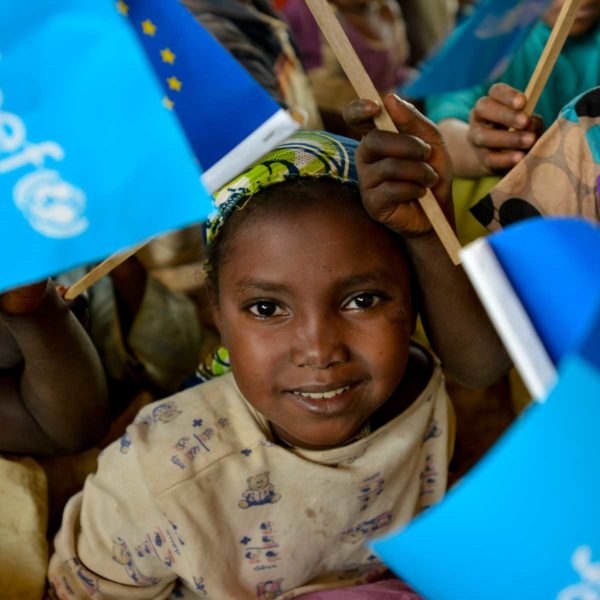 A smiling girl is among children holding and waving Unicef flags in a learning and protection space in Cameroon for refugees from the Central African Republic. Photo: Unicef 2015 Rich