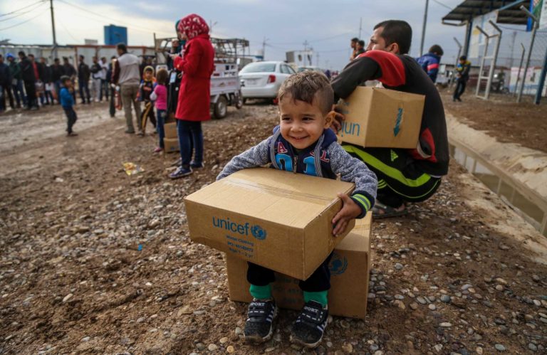 How does Unicef source winter clothes for Syrian children? A young boy clutches a box of Unicef winter clothing kits.