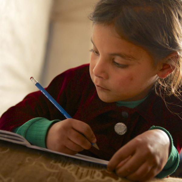 A young child completes homework in the tent she shares with 16 family members, in Dalhamieh, Syria. Photo: UNICEF/2013/Noorani